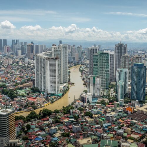 Aerial view of tall office and apartment buildings in downtown Manila. A river bisects the scene.