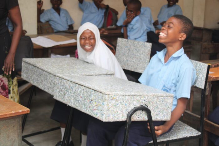 A boy and girl sit side by side in a classroom. Both are in the middle of a hearty laugh.