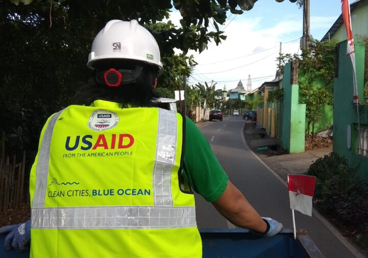 A man wearing a high visibility vest with the USAID logo on the back is facing away from the camera.