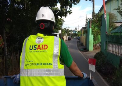 A man wearing a high visibility vest with the USAID logo on the back is facing away from the camera.