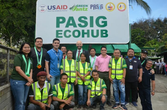 A group of people, some in high-visibility vests and some in normal clothes, pose for the camera in front of a sign that reads "Pasig Ecohub"