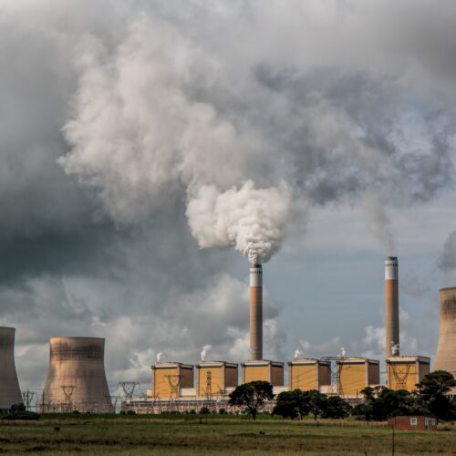 Image: A power station is surrounded by four cooling towers and two smokestacks that are billowing smoke.