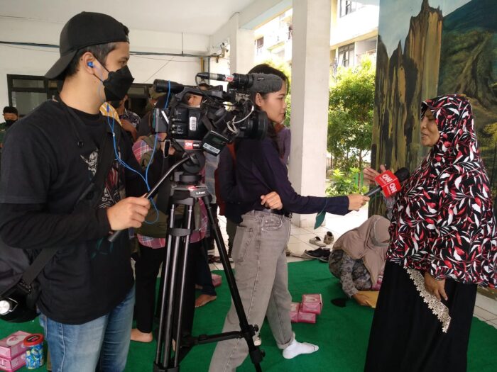 Two journalists with a camera and microphone, interviewing a local woman.