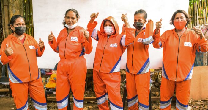 Five women in orange jumpsuits pose for the camera, giving "two thumbs up."