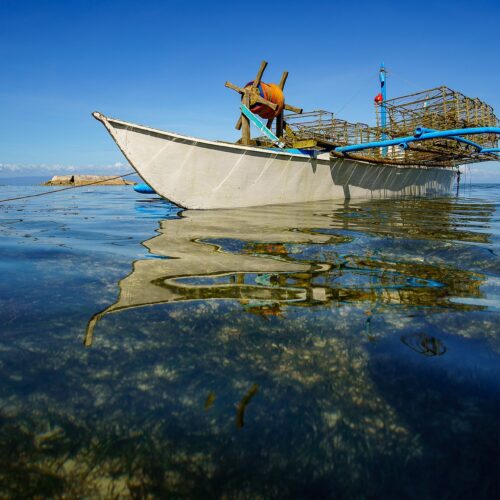 Image of a boat with outriggers taken floating on placid seawater, taken from just above water level.