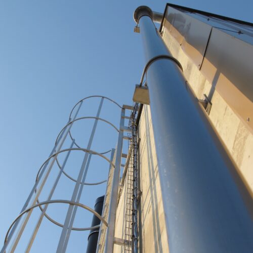 Vertical image of a smokestack on the side of a building and its accompanying ladder.