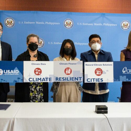 Two men and three women wearing masks stand in front of banners bearing the USAID logo and the words 