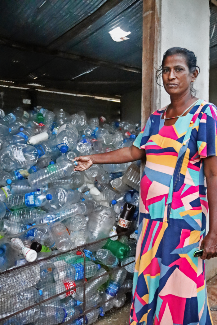 a woman stands next to a bin full of empty plastic bottles