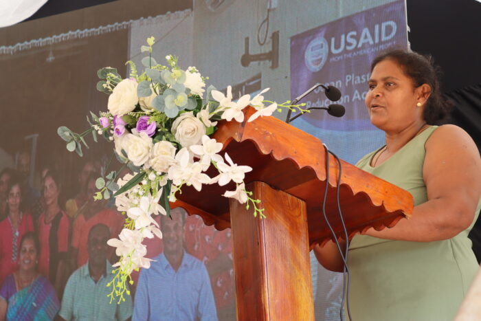 a woman stands at a podium, giving a speech.