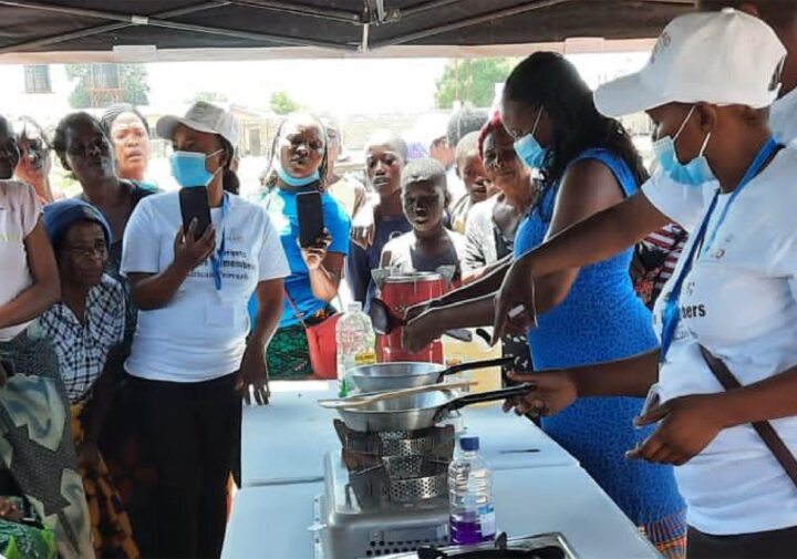 A group of women demonstrates the use of LPG cookstoves to a large group of onlookers.