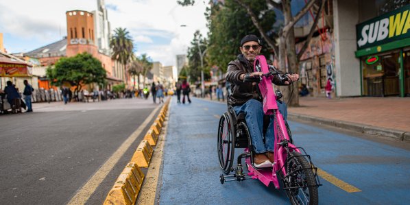A man rides an electric bike toward the camera in a protected bike lane in central Bogotá.