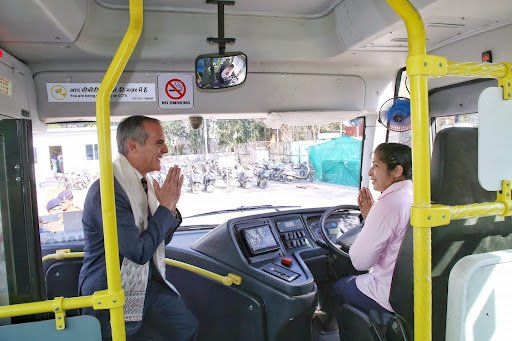 A man boards a bus while greeting the female driver.