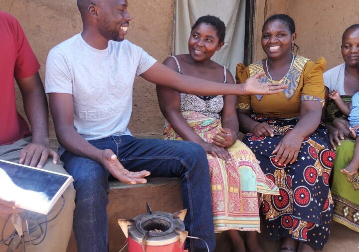 A family poses outside of a house and near a cookstove, smiling at the camera.
