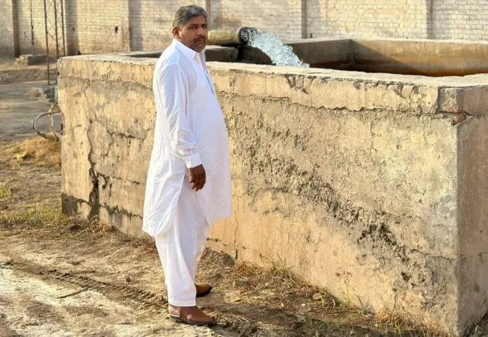 A man stands next to a water tank, looking over his shoulder at the camera.
