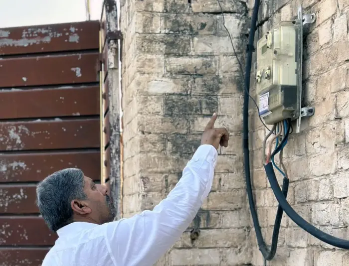 A man points at a electric meter mounted on a brick wall.