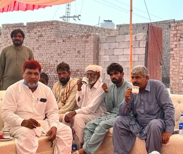 A group of men sit in the shade drinking tea. 