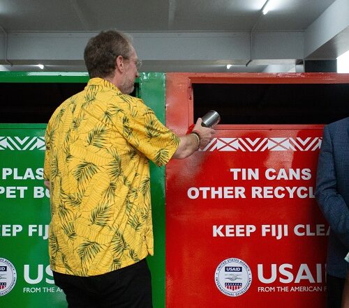 A man tosses a recyclable metal can into a multicolored trash bin.