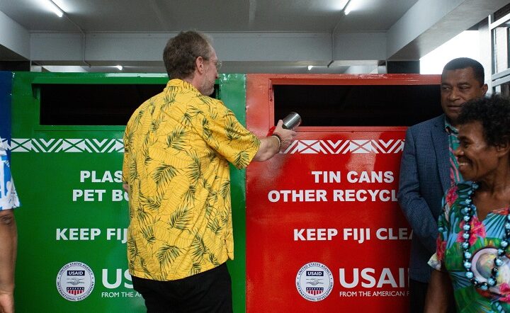 A man tosses a recyclable metal can into a multicolored trash bin.