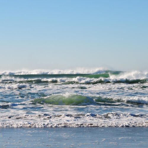 Image: Blue-green waves are crashing on a beach.