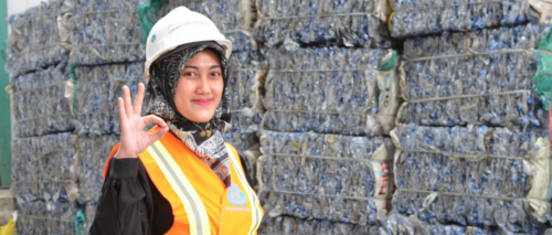 a woman in an orange workers vest standing in front of collected plastic waste