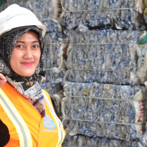 a woman in an orange workers vest standing in front of collected plastic waste