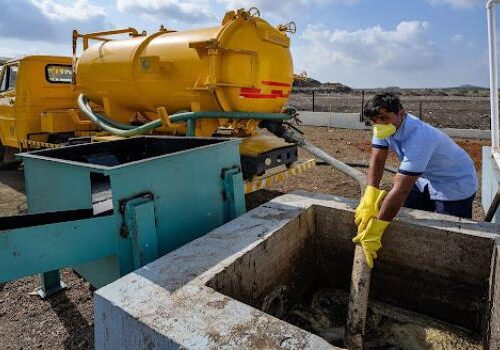 A man wearing a mask and gloves holds a hose into a septic tank.